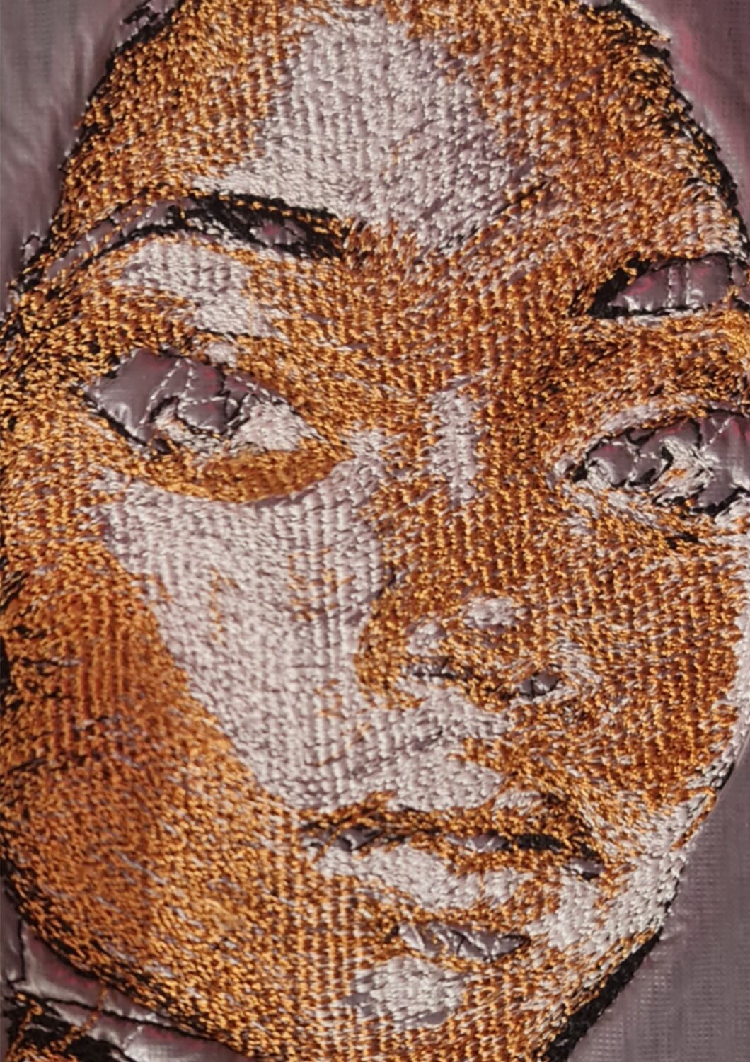Macro close-up of the hand-embroidered portrait, showing individual stitches